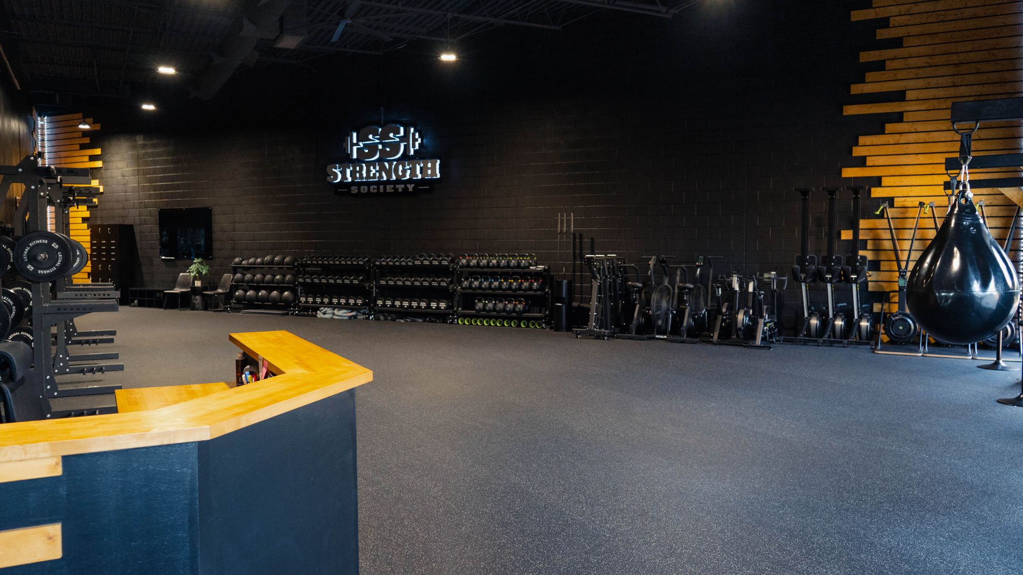 Wide view of the Strength Society studio: an open training floor with weight racks and a punching bag under the studio sign.