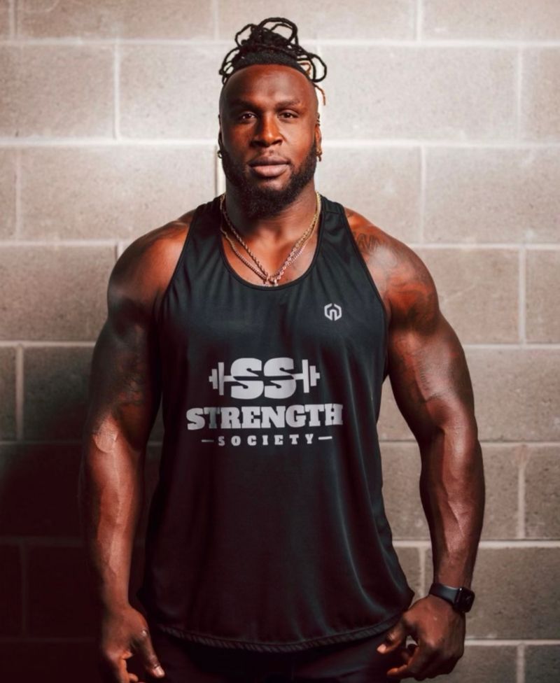 Jonotthan Harrison standing in a Strength Society tank top in front of a brick wall.